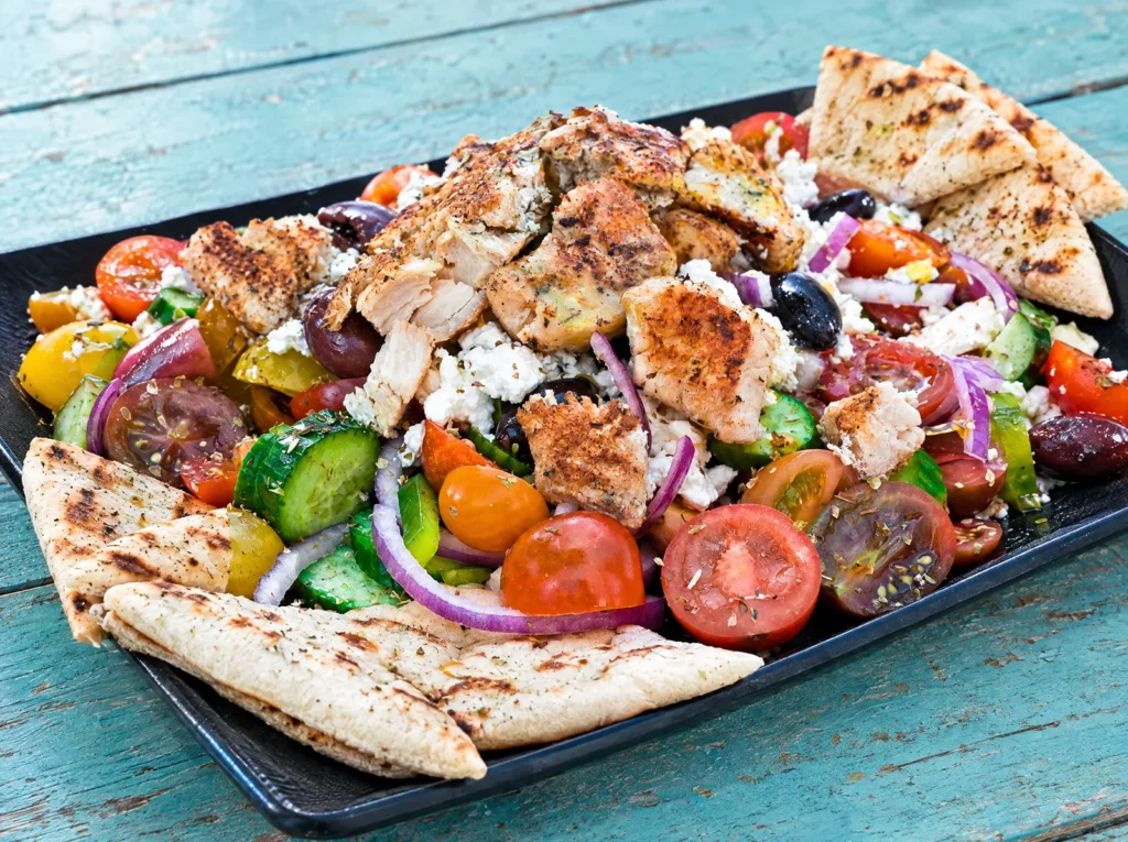 Greek salad with gyro on top and grilled pita